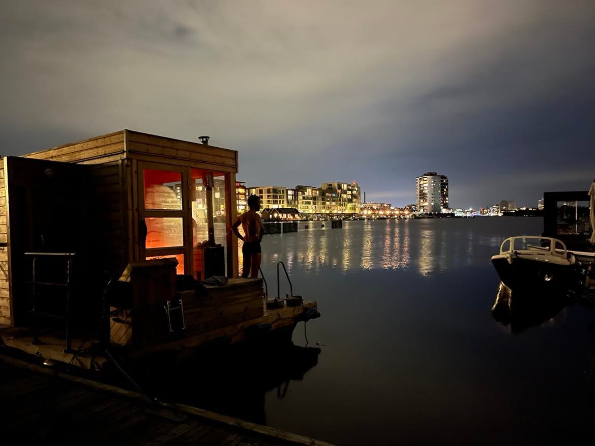 Warm light from Platform’s floating sauna beside Copenhagen’s evening waterfront.